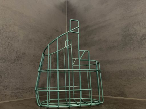 Pulverbeschichtung Maulkorb Drahtgestell in Form einer geometrischen Treppe vor einer grauen Wand.