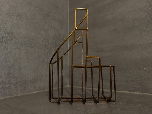 Goldene Treppe aus Metall in minimalistischem Design vor grauer Wand.